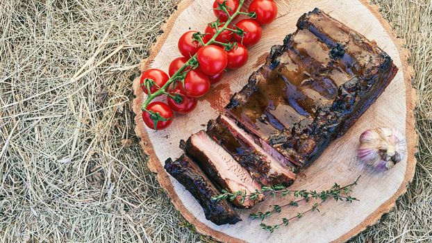 Barbecue ribs meat prepared in traditional European style with rosemary herb cherry tomatoes and garlic on a raw solid wood cutting plate