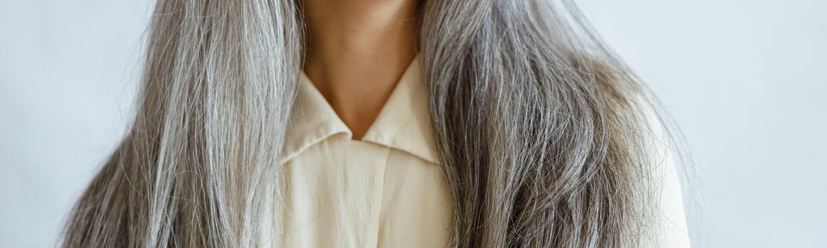 Middle aged woman with long silver hair smiles on light grey background in studio closeup. Mature beauty lifestyle
