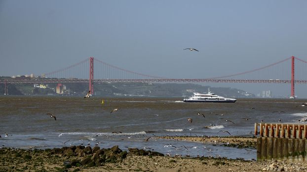 Long shot of 25 de Abril Bridge and boat in Lisbon over Tagus river