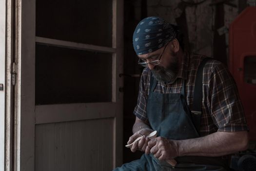 Spoon craft master in his workshop with handmade wooden products and tools working checking curve and line straight. High quality photo