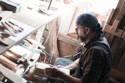 Spoon master in his workshop with wooden products and tools selecting right wood to make wooden kitchenware products. High quality photo