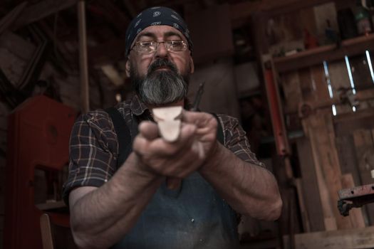 Spoon craft master in his workshop with handmade wooden products and tools working checking curve and line straight. High quality photo