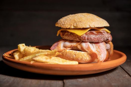 Premium grilled beef hamburger with bacon, cheese and French fries. Delicious American burger on wooden background. High quality photography