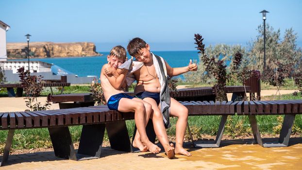 The two boys smile. Children sit on a bench against the sea. Family beach holidays.