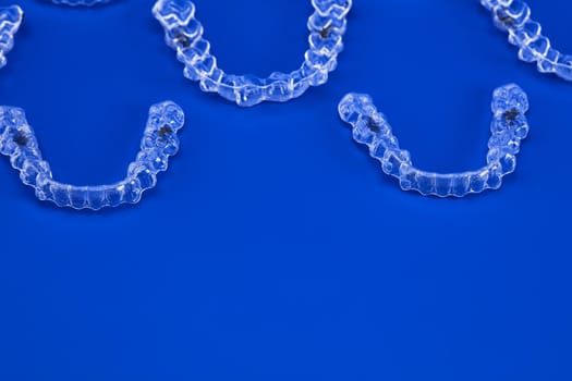 Invisible orthodontics cosmetic brackets on blue background, tooth aligners, plastic braces. A way to have a beautiful smile and white teeth.
