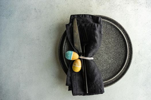 Festive table setting for Easter dinner on concrete background with black cutlery