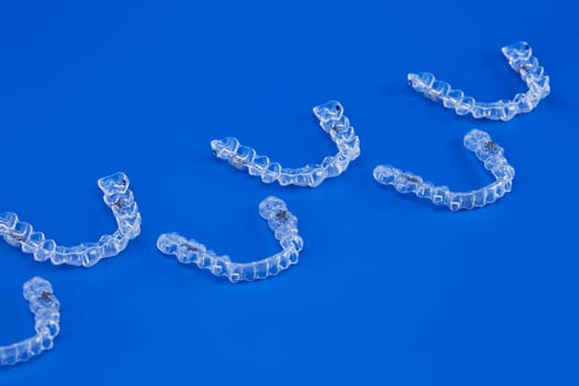 Invisible orthodontics cosmetic brackets on blue background, tooth aligners, plastic braces. A way to have a beautiful smile and white teeth.