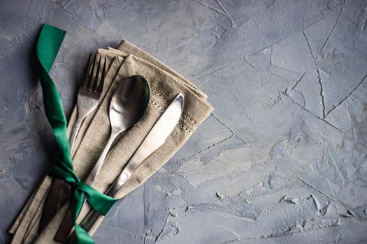 Cutlery set with green ribbon and silverware on linen napkin