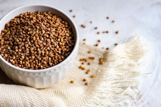 Bowl full of organic raw buckwheat on wooden table with towel