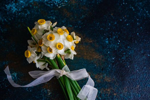 Bouquet of fresh spring daffodil flowers with ribbon on stone background