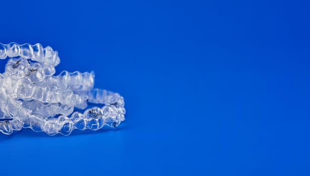 Invisible orthodontics cosmetic brackets on blue background, tooth aligners, plastic braces. A way to have a beautiful smile and white teeth.