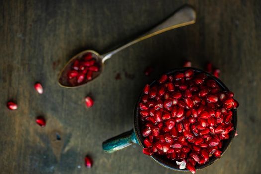 Ripe organic pomegranate fruit on the ceramic cup and vintage spoon on wooden table