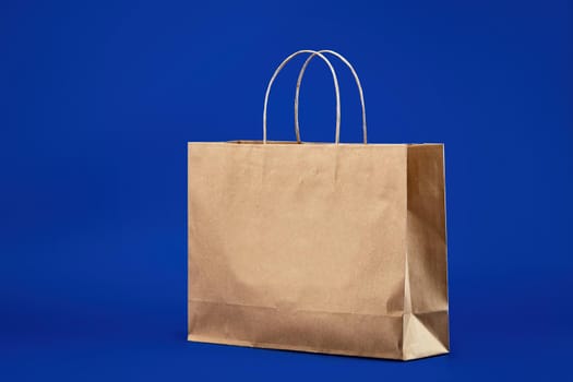 Blank brown paper carrier bag with handles for shopping. Paper bag on a blue background, responsible attitude to the environment. Environmental packaging.