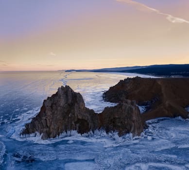 Frozen Lake Baikal, Cape Burhan Shaman rock of Olkhon Island. Tourists on lake Baikal, walking on the ice.. The famous natural landmark Russia. Blue transparent ice with deep cracks.