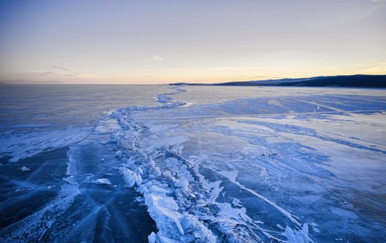 Frozen Lake Baikal, Lake Baikal hummocks. Beautiful winter landscape with clear smooth ice near rocky shore. The famous natural landmark Russia. Blue transparent ice with deep cracks.