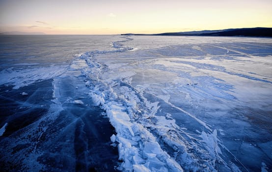 Frozen Lake Baikal, Lake Baikal hummocks. Beautiful winter landscape with clear smooth ice near rocky shore. The famous natural landmark Russia. Blue transparent ice with deep cracks.