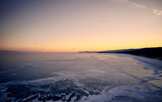 Frozen Lake Baikal, hummocks. Beautiful winter landscape with clear smooth ice near rocky shore. The famous natural landmark Russia. Blue transparent ice with deep cracks.