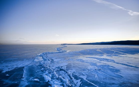 Frozen Lake Baikal, Lake Baikal hummocks. Beautiful winter landscape with clear smooth ice near rocky shore. The famous natural landmark Russia. Blue transparent ice with deep cracks.