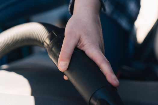 Hand of young girl in blue shirt and jeans vacuuming car seat. Detail shot of hand in strong natural light from outside.