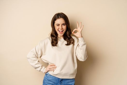 Excellent. Smiling beautiful woman showing okay, ok zero sign, approve smth good, praising and complimenting, beige background.