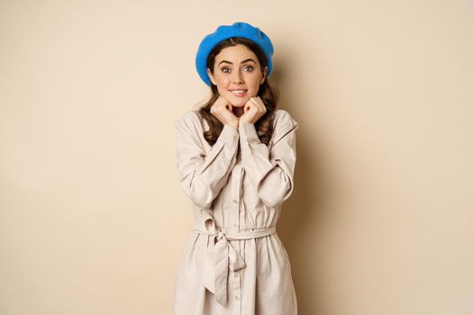 Portrait of beautiful woman in trendy outfit, touching her face and looking dreamy, yearning smth, standing against beige background. People concept