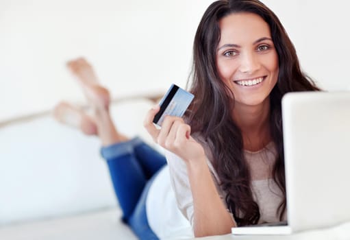 Portrait of a young woman holding a credit card while using a laptop.