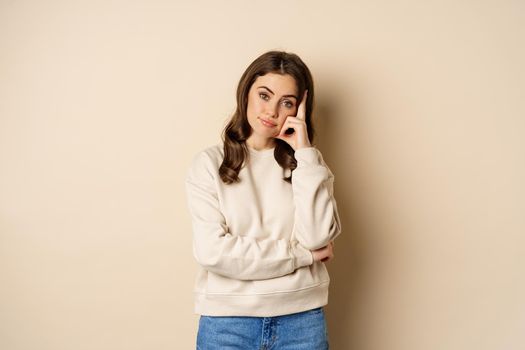 Annoyed woman, roll eyes and looking unamused, bothered and bored, standing over beige background.