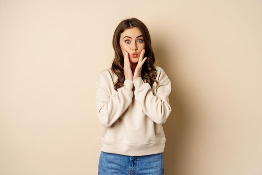 Excited beautiful woman looking amazed, checking out big news, special promo offer, standing amused over beige background.