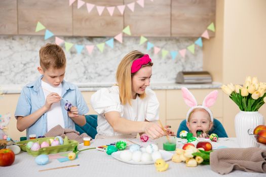 Big Happy Family preparing for Easter. Cute children with mother painting eggs. Home activity. Concept of unity and love. Mom, son, daughter. Brother and sister