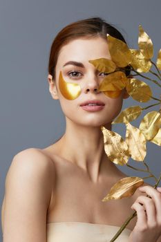 portrait woman golden leaves luxury skin care face patches bare shoulders isolated background. High quality photo