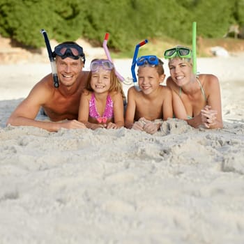 A family in snorkeling gear lying on the sand at the beach.