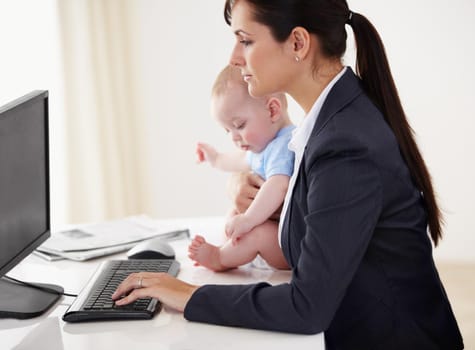 Young working mother holding a baby while working on her computer.