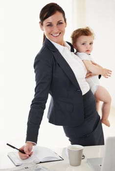 Working mother holding her baby while smiling and signing a document.