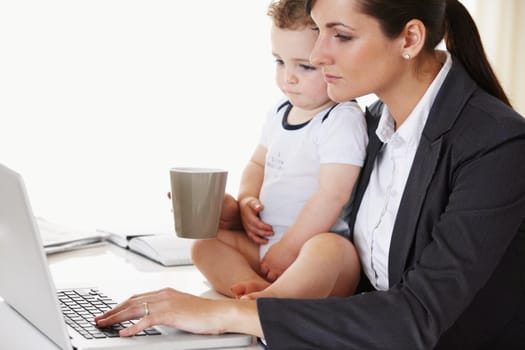 Young working mother holding a baby while working and drinking coffee.