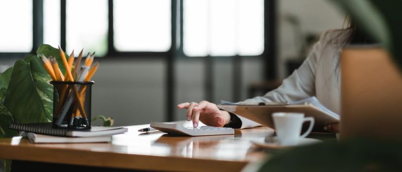 Close up of businesswomen or accountant using calculator calculate while working analytic business report on the workplace, Planning financial and accounting concept.