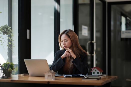 Concept of property investment, Mortgage and real estate residental house. business asian female using laptop with wooden house.