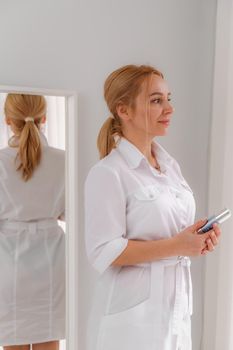 A blonde woman in white formal clothes looks out the window and is reflected in the mirror. On a white background