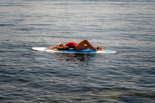 Sporty girl on a glanders surfboard in the sea on a sunny summer day. In a striped swimsuit, he lies on his back. Summer activities by Stortom by the sea.