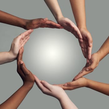 Cropped shot of a group of hands linking together to form a circle against a grey background.