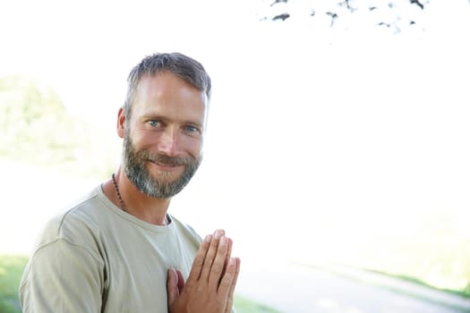 Portrait of a handsome mature man standing with his hands in prayer position outdoors.