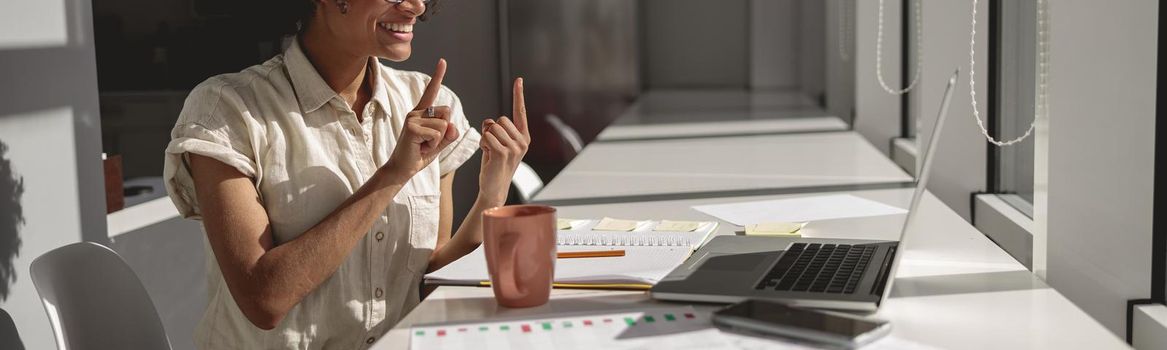 Happy pretty lady learning and communicating in sign language online while sitting in the office