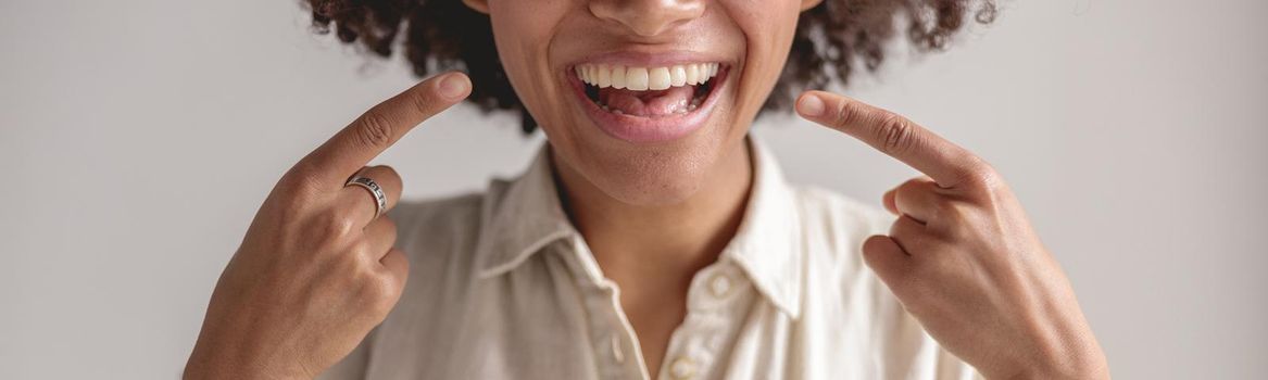 Cropped photo of happy African American woman pointing her fingers at smile, isolated on grey background