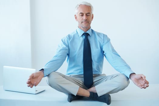 Full length shot of a mature businessman sitting cross legged and meditating.