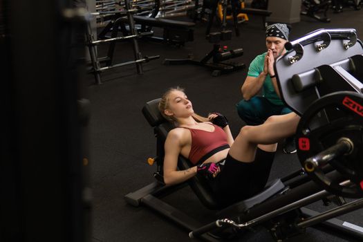 RUSSIA, MOSCOW - FEB 11, 2022: A girl is engaged in a led press simulator in a red blonde beautiful on a black background leg gym training press flexing, for lifestyle young for fit and bodybuilding bodybuilder, white length. Woman slim beautiful, leisure trainer