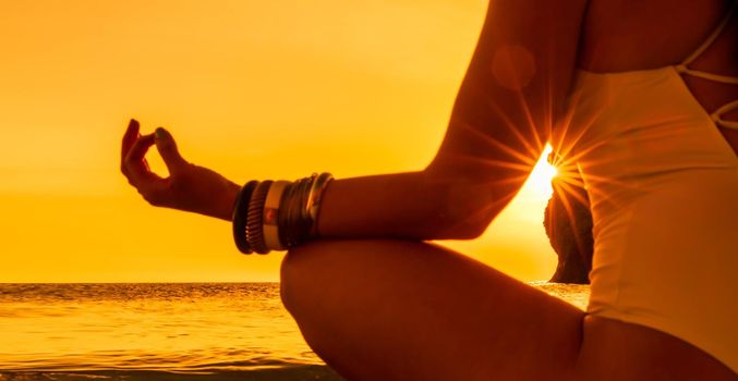 Banner. Young woman practicing yoga on the beach with sunset. Keeps fingers connected, the sun shines through them. The concept of a healthy lifestyle, harmony