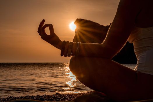 Young woman practicing yoga on the beach with sunset. Keeps fingers connected, the sun shines through them. The concept of a healthy lifestyle, harmony