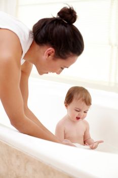 A mother washing her cute baby girl in the bath.