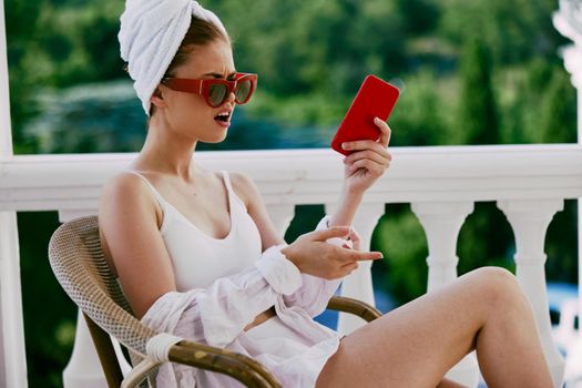 Portrait of young woman in sunglasses sits on the balcony and uses the phone Perfect sunny morning. High quality photo