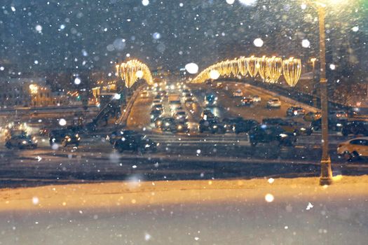 Falling snow against the backdrop of cars with headlights on at night in the center of Moscow. The concept of the first snow or snowfall in winter.