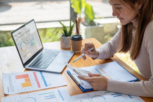 Asian woman using calculator for analysis maketing plan, Accountant calculate financial report, computer with graph chart. Business, Finance and Accounting concept
